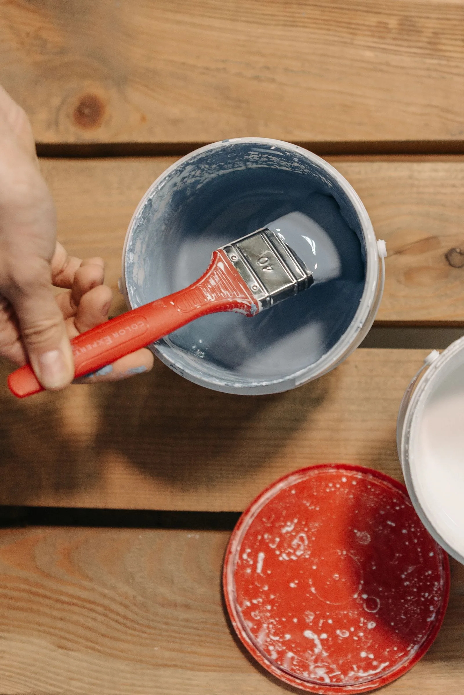 Hand holding a paintbrush dipped in blue paint over a wooden surface, painting furniture with chalk paint
