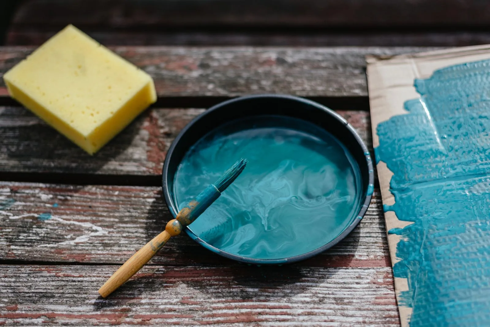 Turquoise paint mixed in a bowl with a brush on a wooden board, ready for a milk paint furniture project