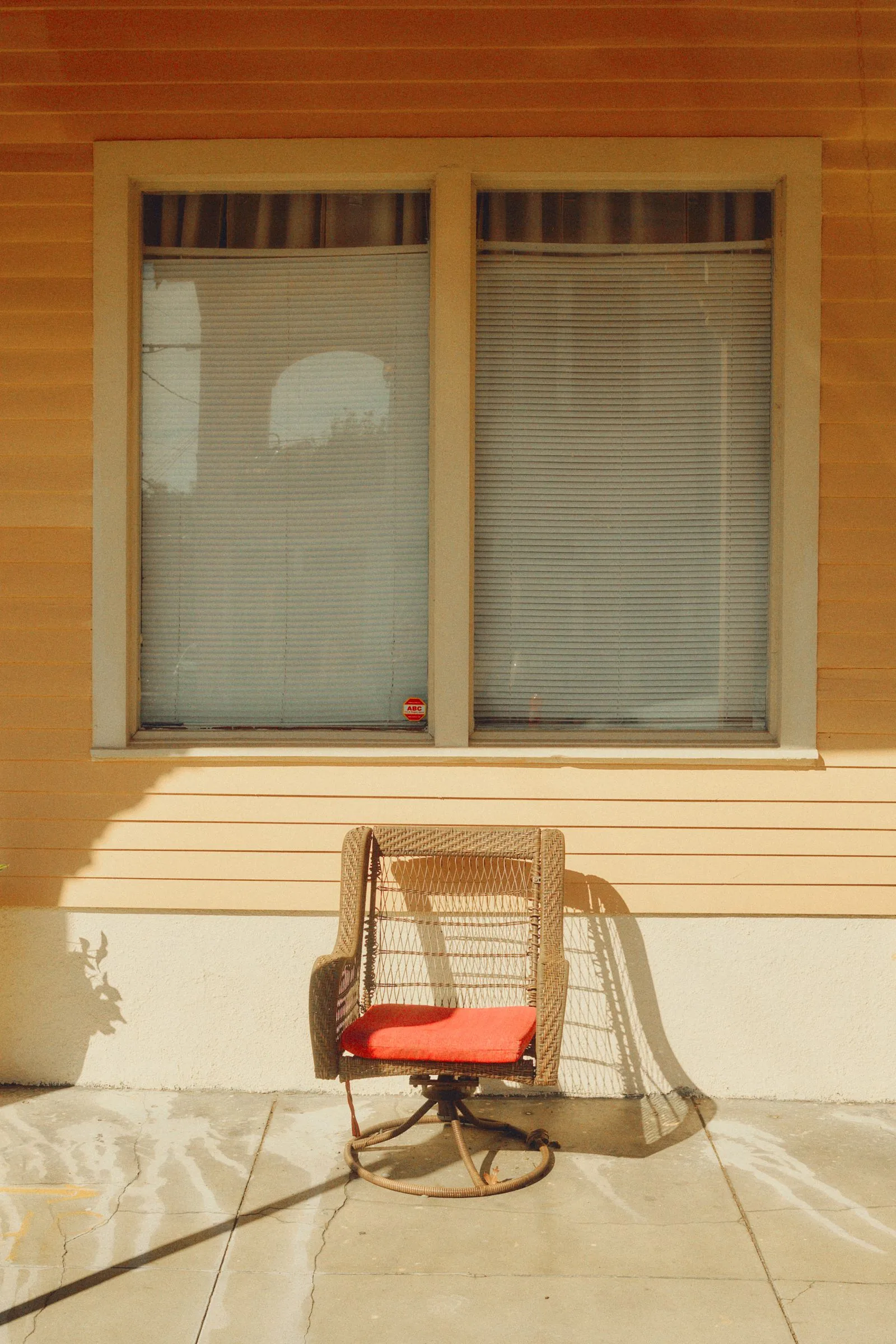 Wicker chair with a red cushion on a sunny porch, the kind of piece people repaint with spray paint