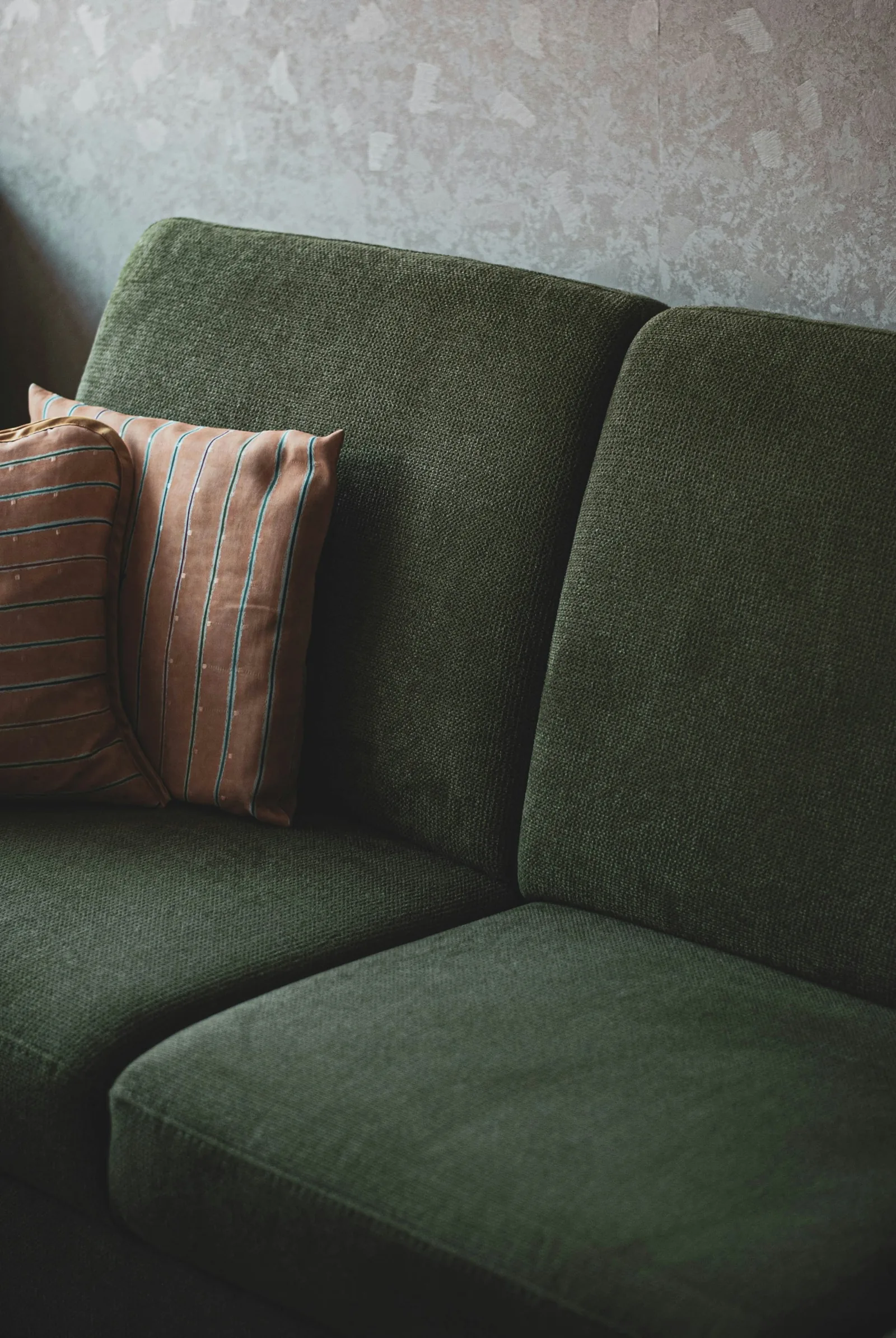 Dark green textured sofa with two striped cushions, an example of couch cushions that need firm foam